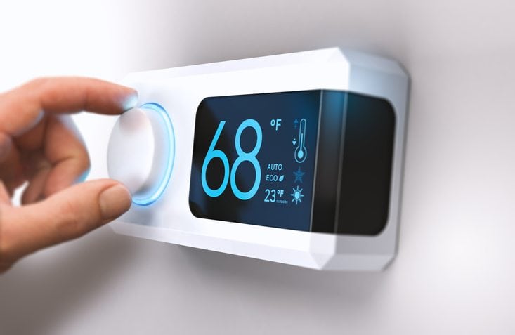 Hand turning a home thermostat knob to set temperature on energy saving mode. fahrenheit units. Composite image between a photography and a 3D background.